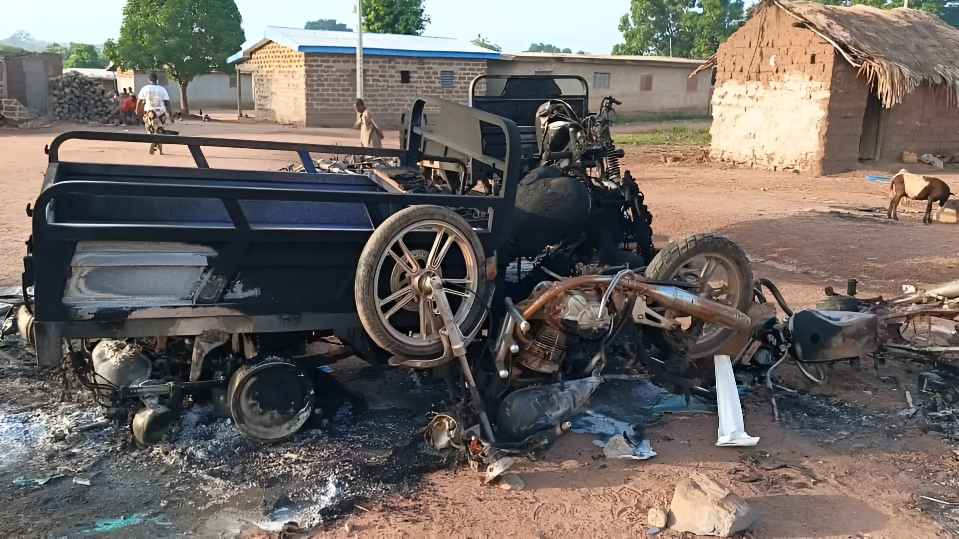 A burned out truck and motorcycle in the middle of a village