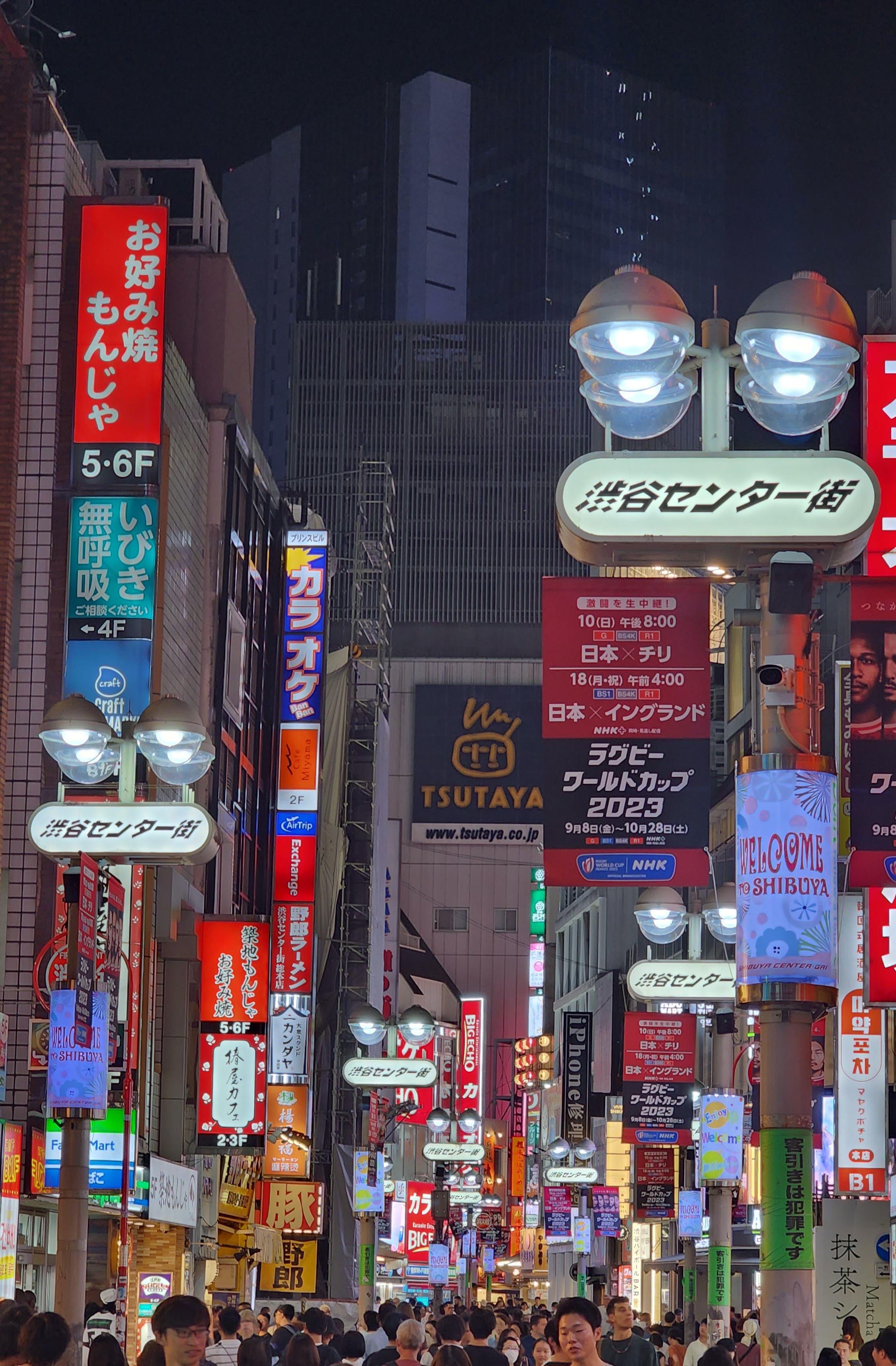 A busy Tokyo street at night, illuminated by neon signs, and full of people walking.